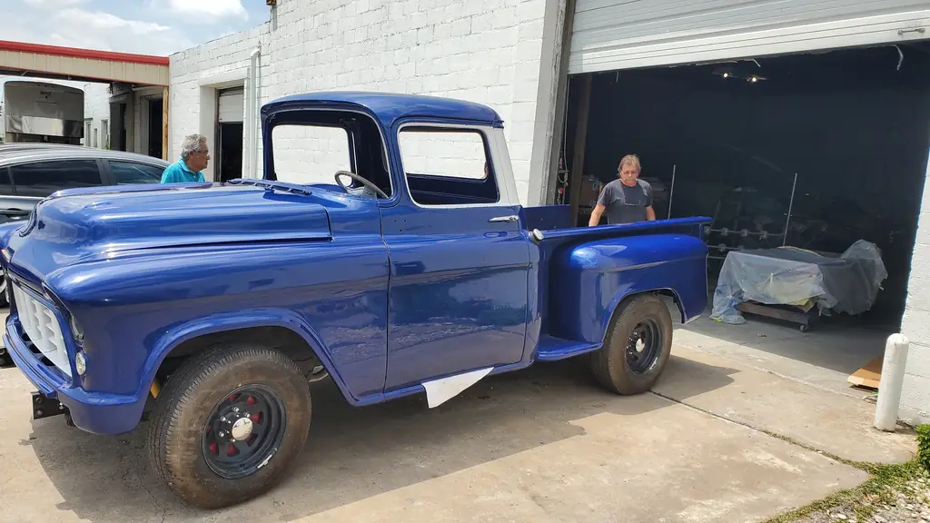 The finished blue pickup parked outside the open bays at the shop